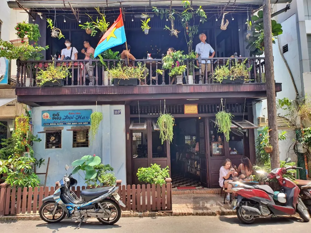 Exterior of Cà Phê Đỗ Phủ cafe at 113A Dang Dung Street with a wooden balcony, hanging plants, motorbikes, and customers.