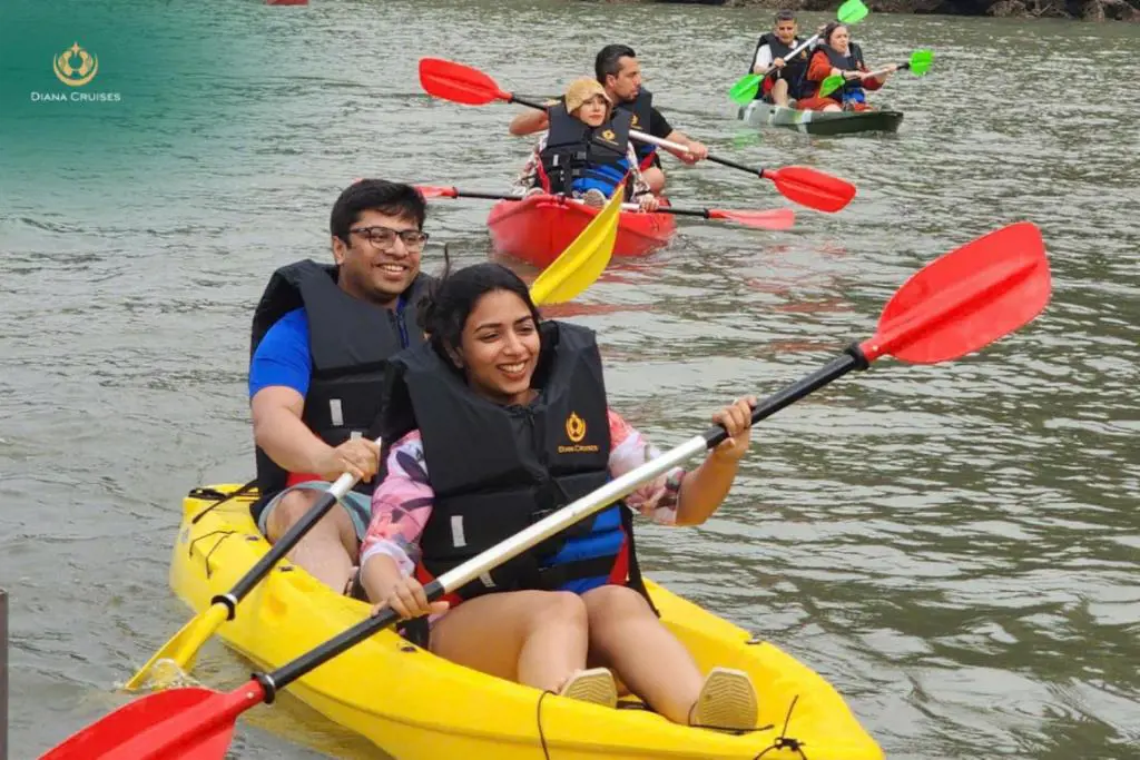A man and woman smiling in a yellow kayak on calm green water while wearing life jackets.