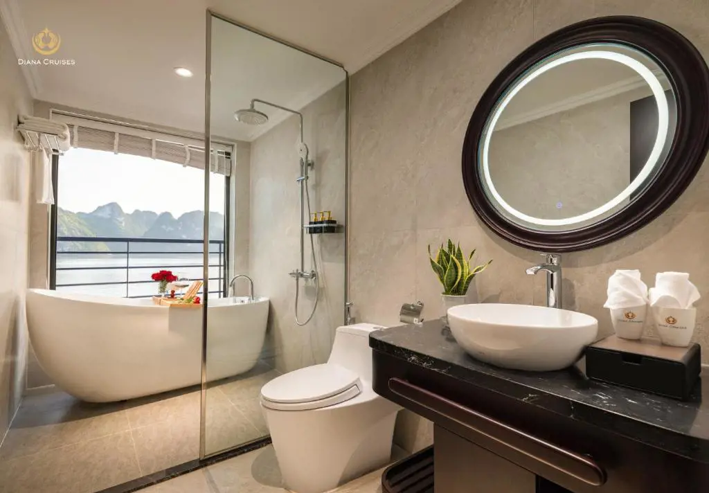 Modern bathroom in an Executive Suite on Diana Cruises, featuring a freestanding bathtub with scenic bay views, glass shower, vessel sink, and backlit round mirror.