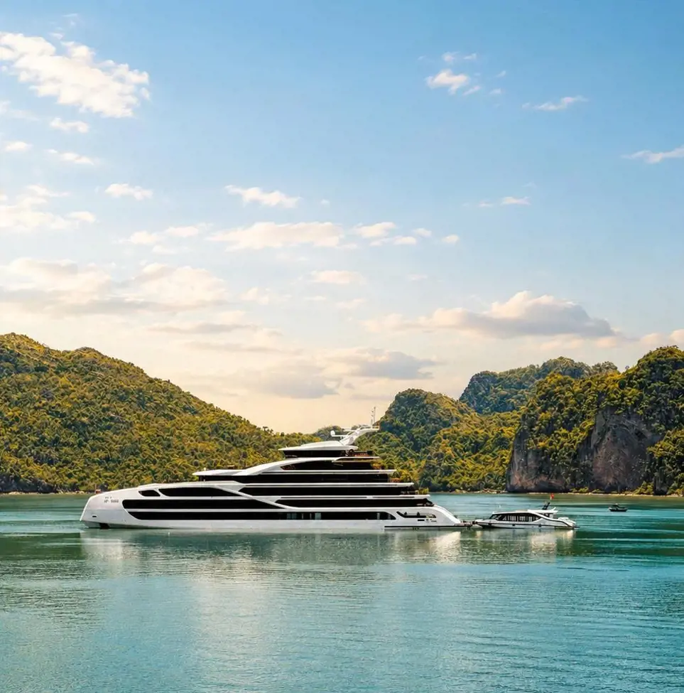 A multi-deck white luxury cruise ship anchored on calm water surrounded by green limestone karst mountains in Ha Long Bay.