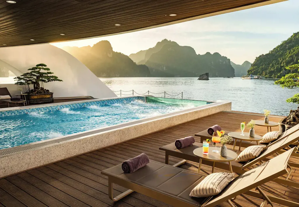 Bể bơi Jacuzzi trên boong du thuyền cao cấp với dãy ghế tắm nắng, đồ uống và tầm nhìn ra vịnh biển hùng vĩ.