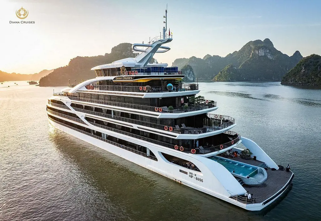 Aerial view of the white multi-deck Diana Cruises ship with an aft swimming pool cruising near limestone karst islands in Ha Long Bay.