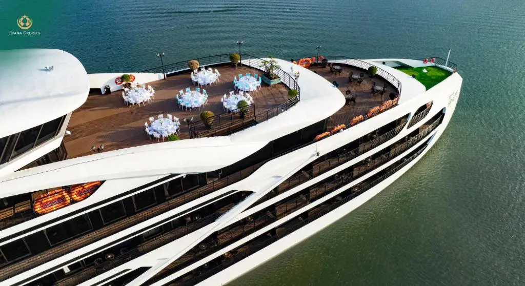High-angle view of the top deck of Diana Cruises ship with round dining tables set up with white tablecloths on open green water.