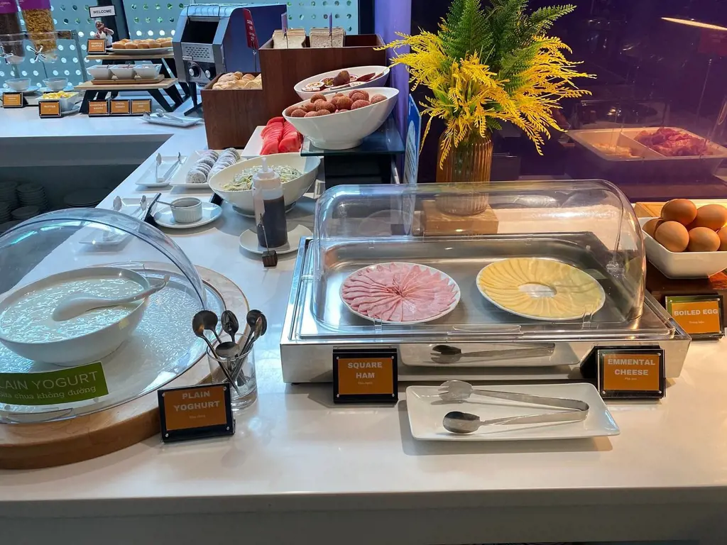 Quầy buffet phục vụ bữa sáng với thịt nguội, phô mai, sữa chua và trái cây tươi tại khách sạn Tru by Hilton Da Nang City Centre