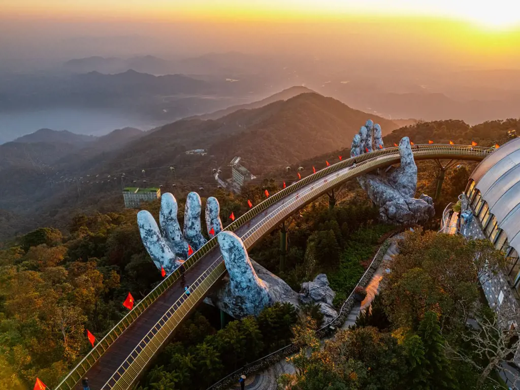 Toàn cảnh Cầu Vàng ở Bà Nà Hills, Đà Nẵng, với lối đi cong được hai bàn tay đá khổng lồ nâng đỡ giữa núi rừng vào lúc hoàng hôn.