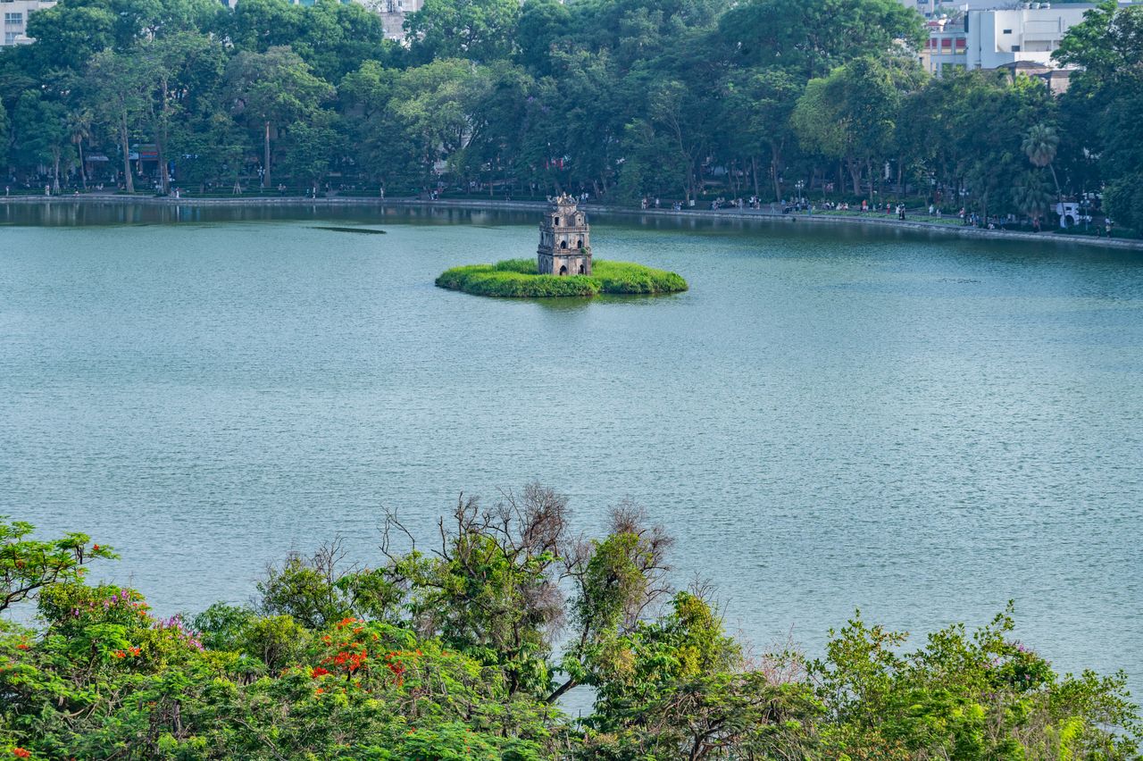 High-angle view of Turtle Tower on a small island in Hoan Kiem Lake, Hanoi, surrounded by calm green water and dense foliage.