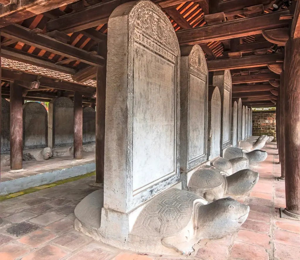 Row of ancient stone stelae carved on turtle pedestals beneath a traditional wooden pavilion roof at the Temple of Literature in Hanoi.