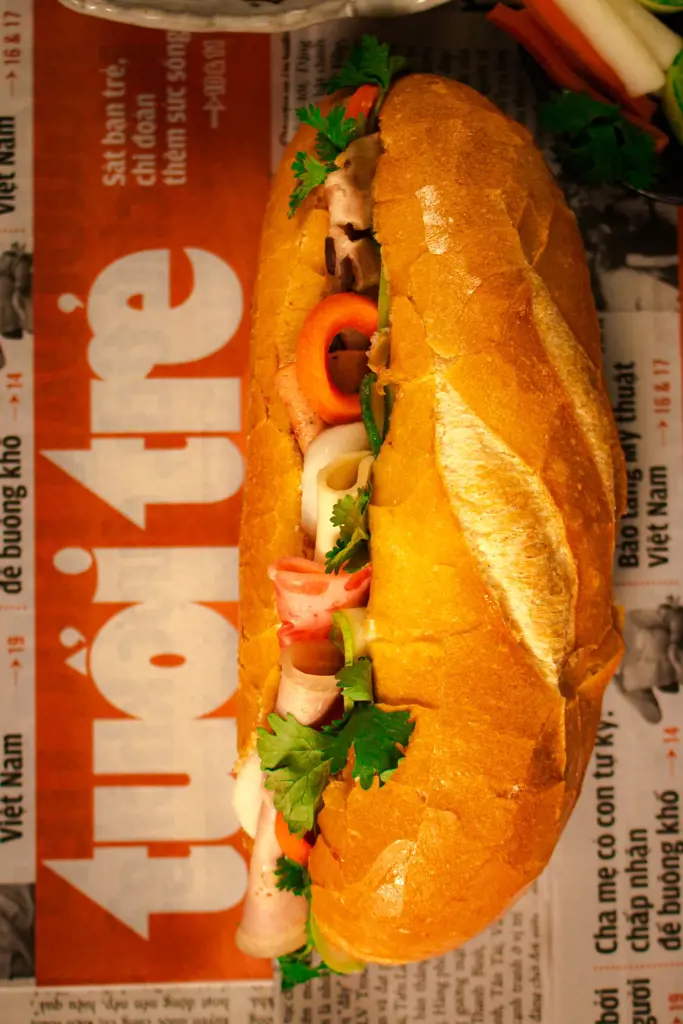 A crusty golden baguette filled with sliced meats, pickled carrots, cucumber, and fresh cilantro leaves.