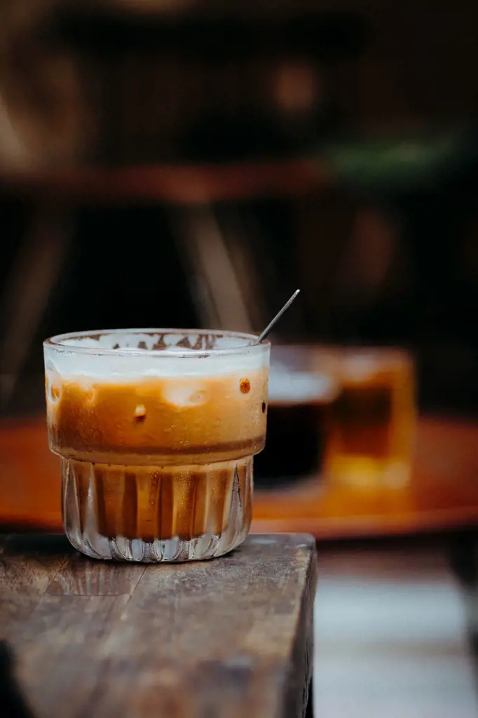 A ribbed glass tumbler filled with iced milk coffee and ice cubes on a wooden surface.