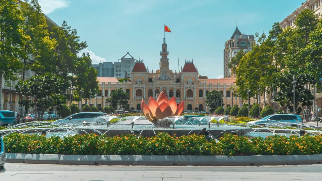Lotus flower fountain spraying water in a landscaped circle on Nguyen Hue Pedestrian Street with Ho Chi Minh City Hall in the background.