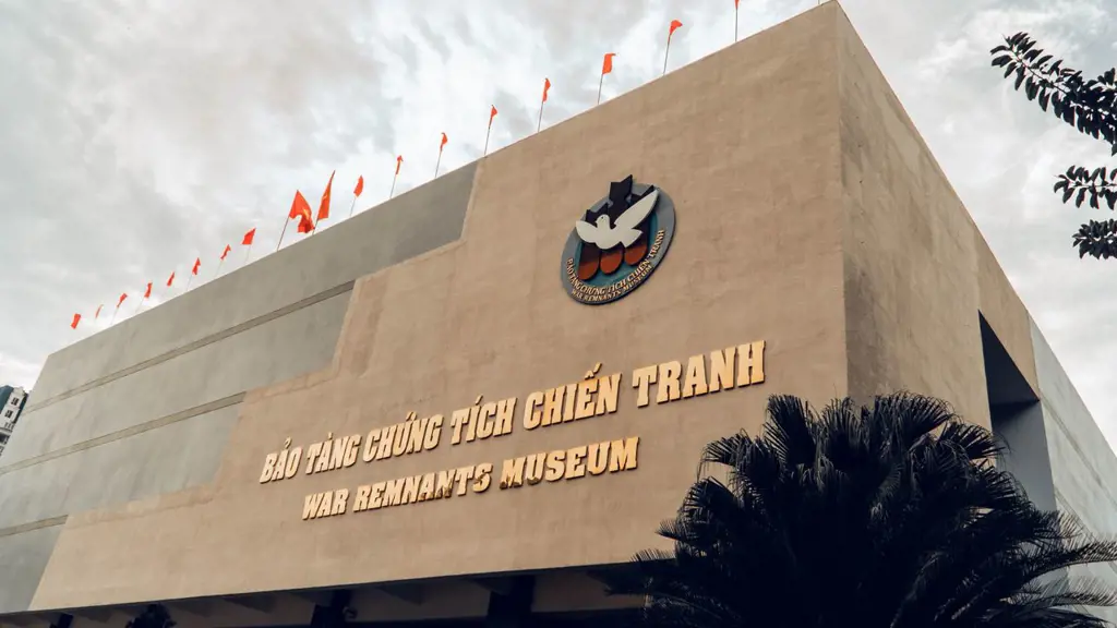 Facade of the War Remnants Museum showing golden lettering in Vietnamese and English alongside a dove emblem and red flags against a cloudy sky.