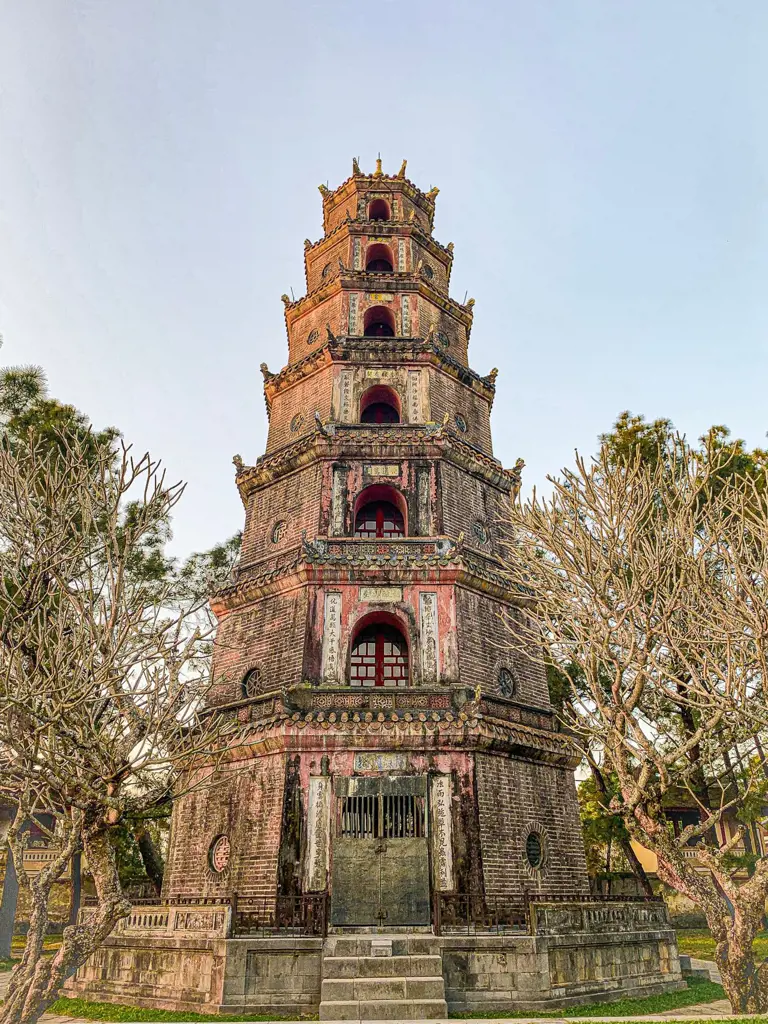 Seven-story octagonal brick pagoda tower flanked by bare frangipani trees.