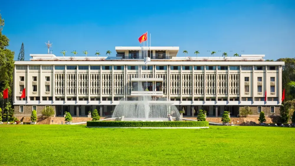 Front facade of the Independence Palace in Ho Chi Minh City with a lush green lawn and central water fountain under a clear blue sky.