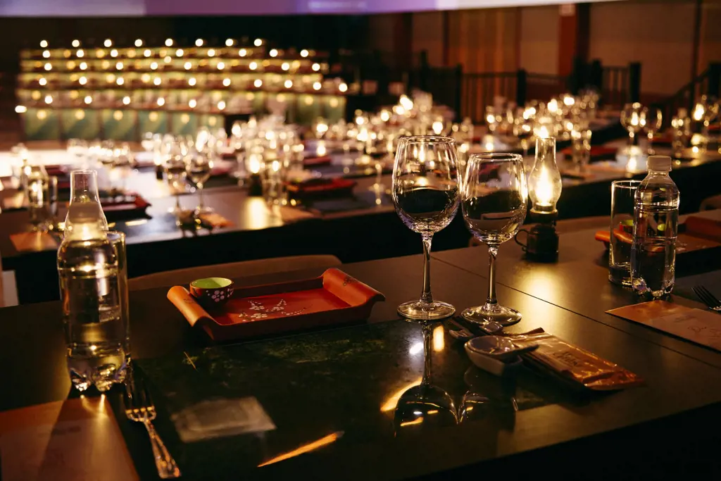 Close-up view of a banquet table set with wine glasses, water bottles, and oil lamps emitting a warm golden glow.