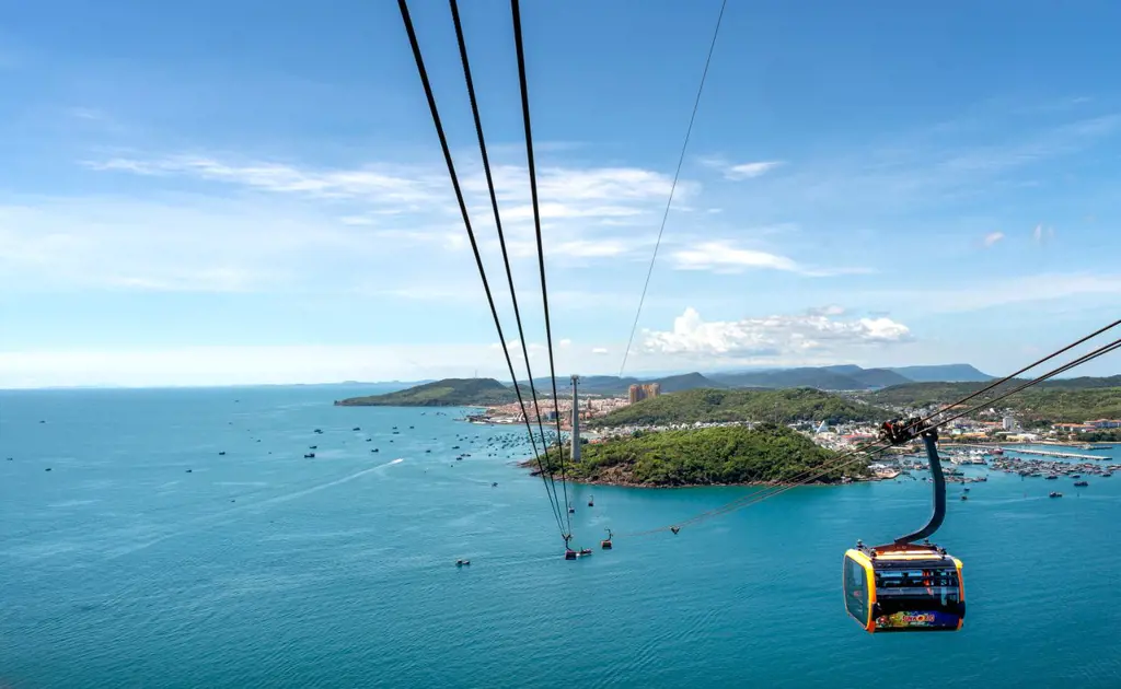 A cable car cabin glides along steel cables over vibrant turquoise ocean waters near the coast of Phu Quoc Island.