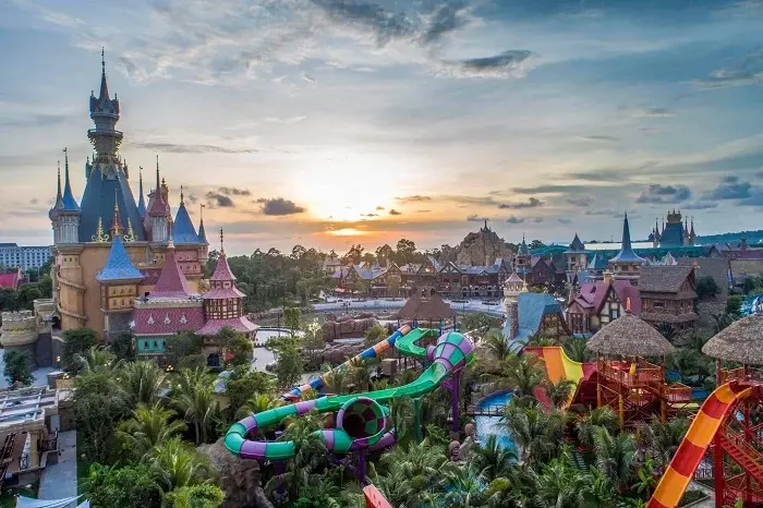 Panoramic sunset view of VinWonders Phu Quoc theme park, featuring a fairytale castle, colorful water slides, and European-style buildings surrounded by palm trees.