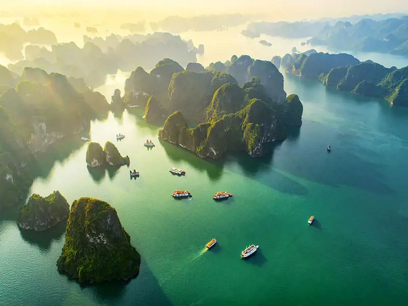 Aerial view of green limestone islets and cruise boats floating on emerald water in Lan Ha Bay, Vietnam.