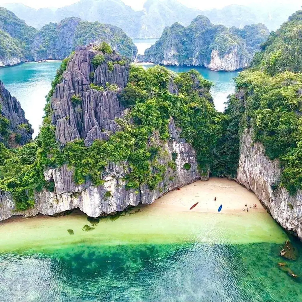 Aerial view of a hidden sandy beach enclosed by steep limestone karst mountains and clear turquoise water.
